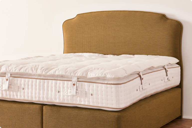 A luxury Vispring mattress topper laid out and secured to a white mattress on top of a mustard brown headboard and divan set